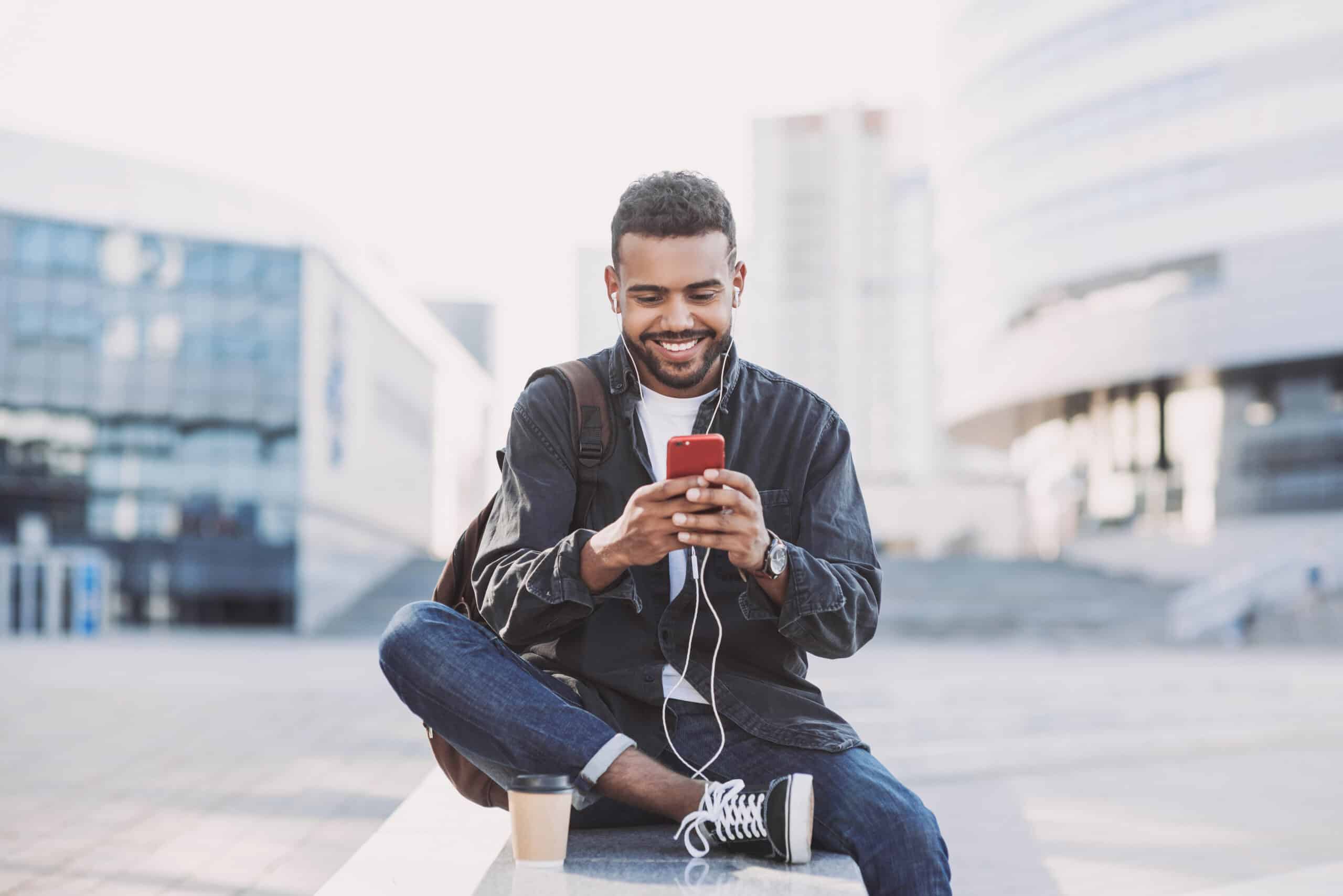 Young handsome men using smartphone in a city. Smiling student man texting on his mobile phone. Coffee break. Modern lifestyle, connection, business concept