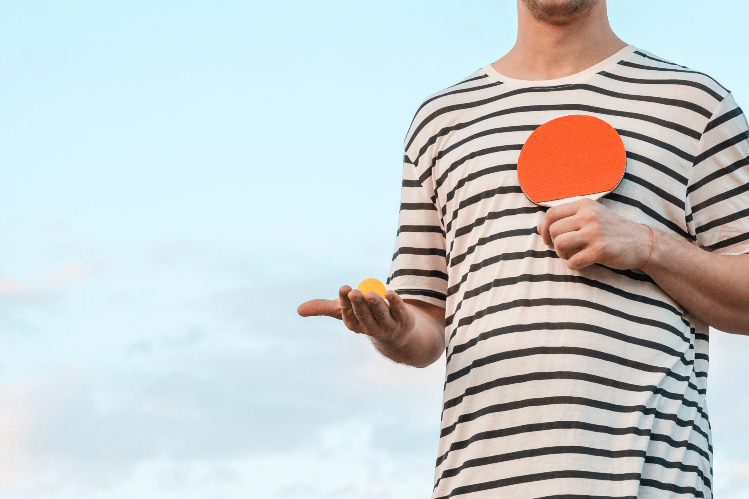 A man in a striped shirt holding a ping pong ball and ping pong paddle