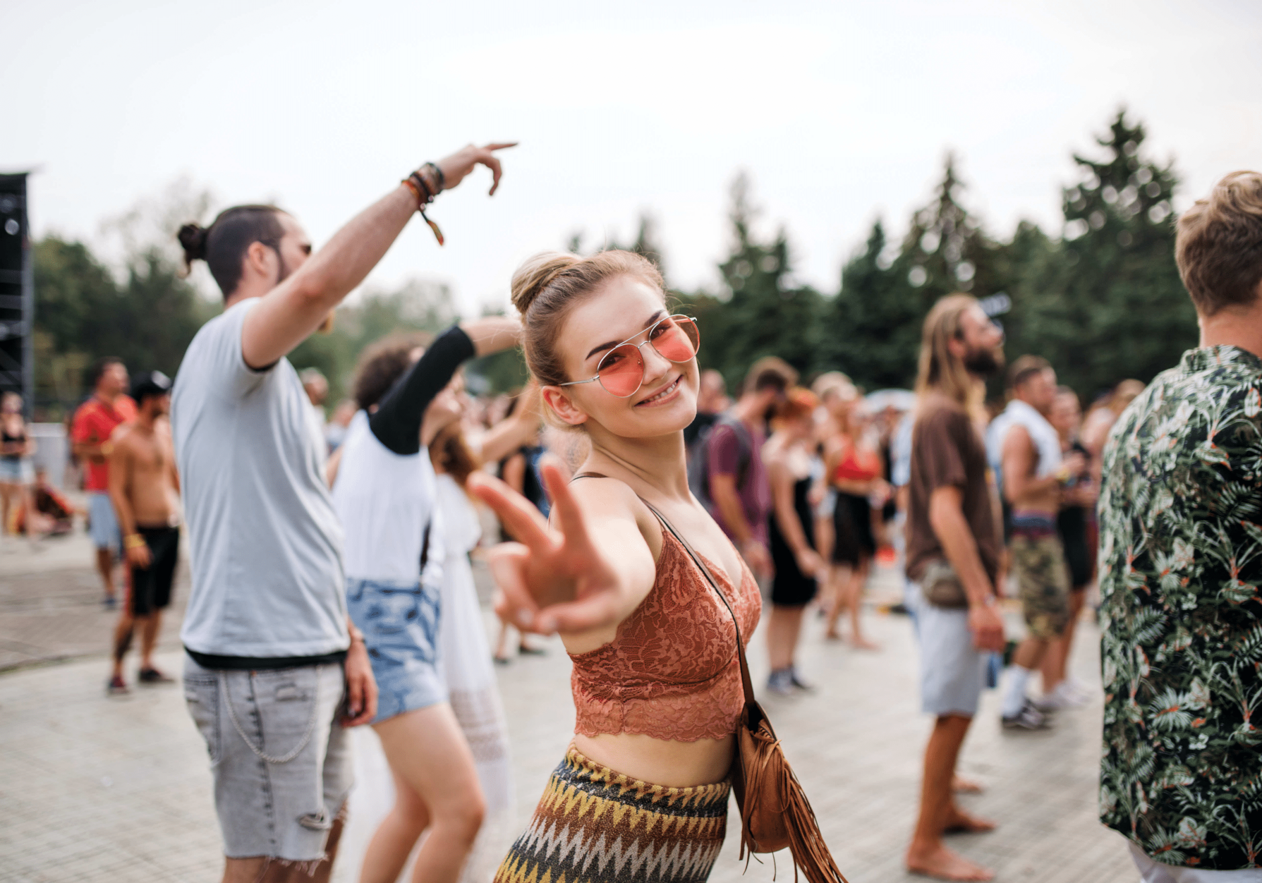 a college girl wearing sunglasses and making a peace sign as she jams out at a festival with other college students