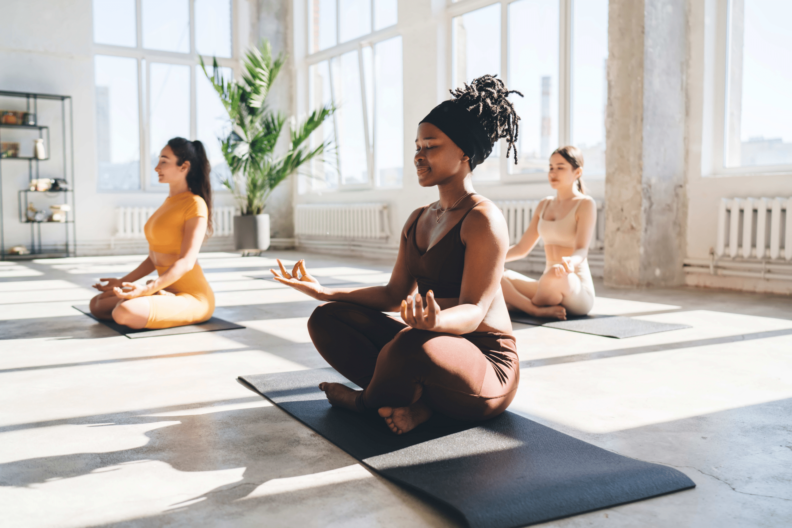 Three female college students sitting on yoga mats with their legs crossed and eyes closed