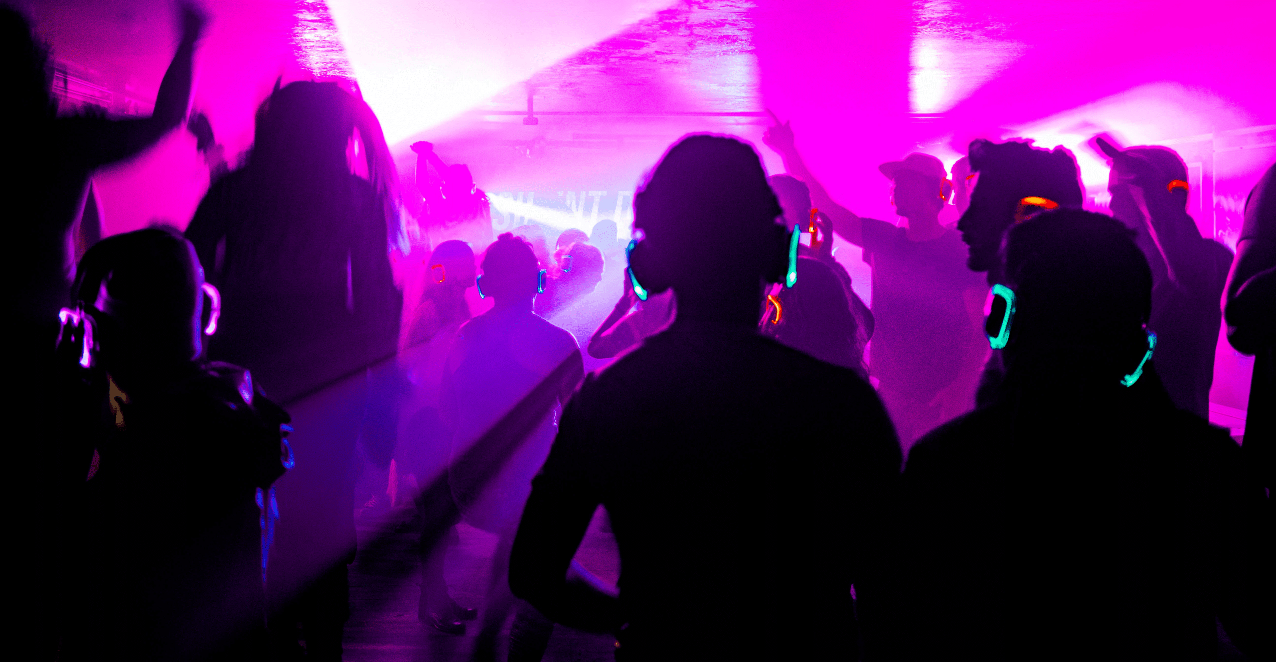 Group of college students dancing with glowing headphones on and neon lights streaming around them