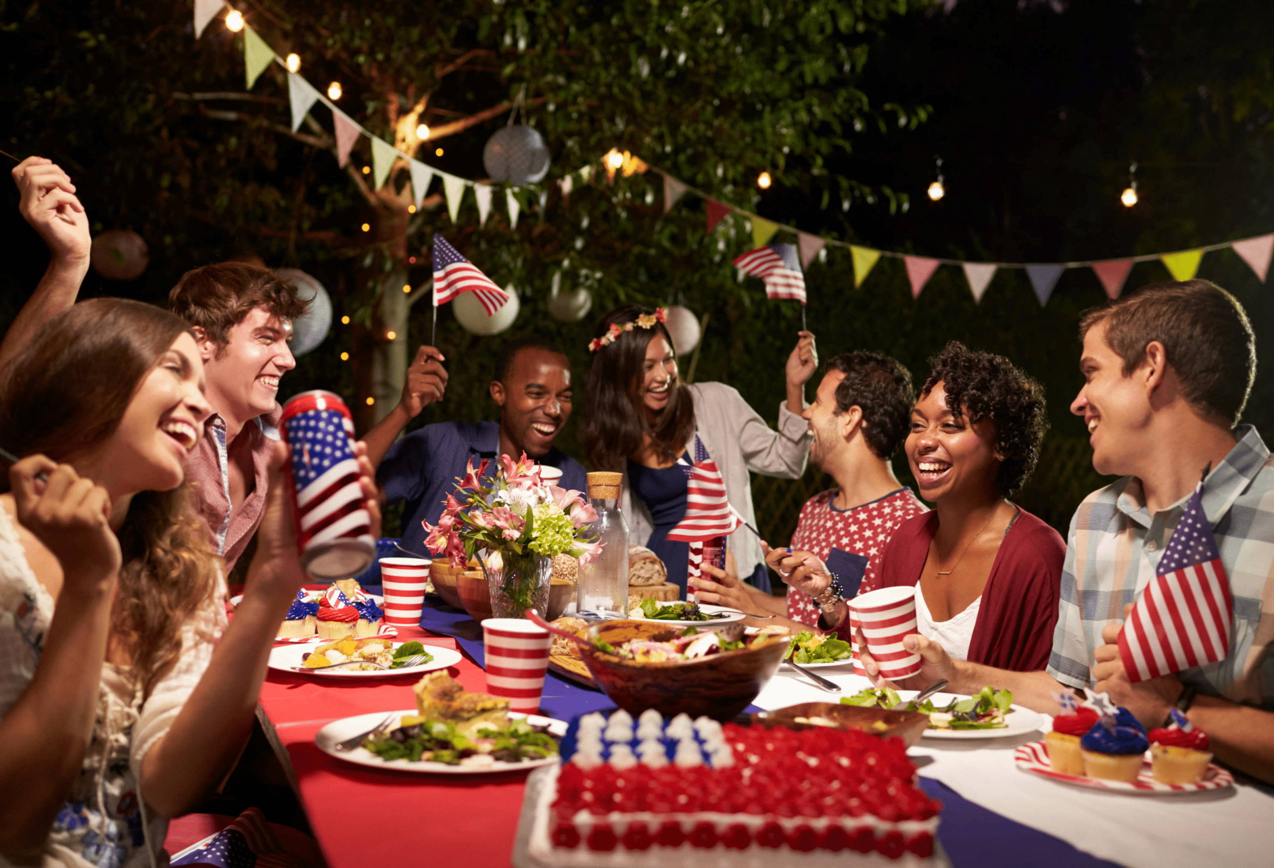 group of people laughing while at a dinner table of red, white, and blue for a fourth of july party