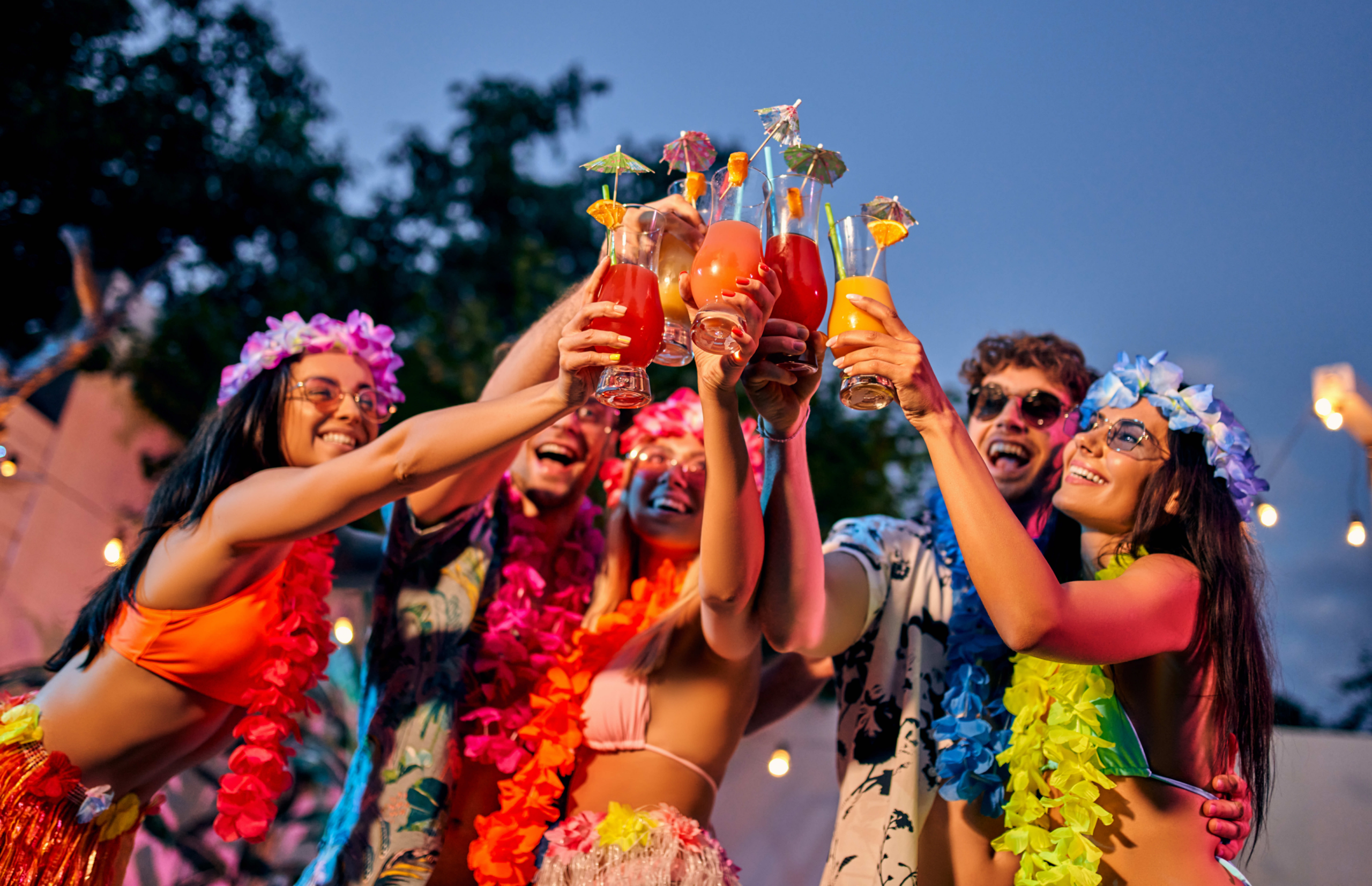 young people cheering cocktail drinks at a tropical party