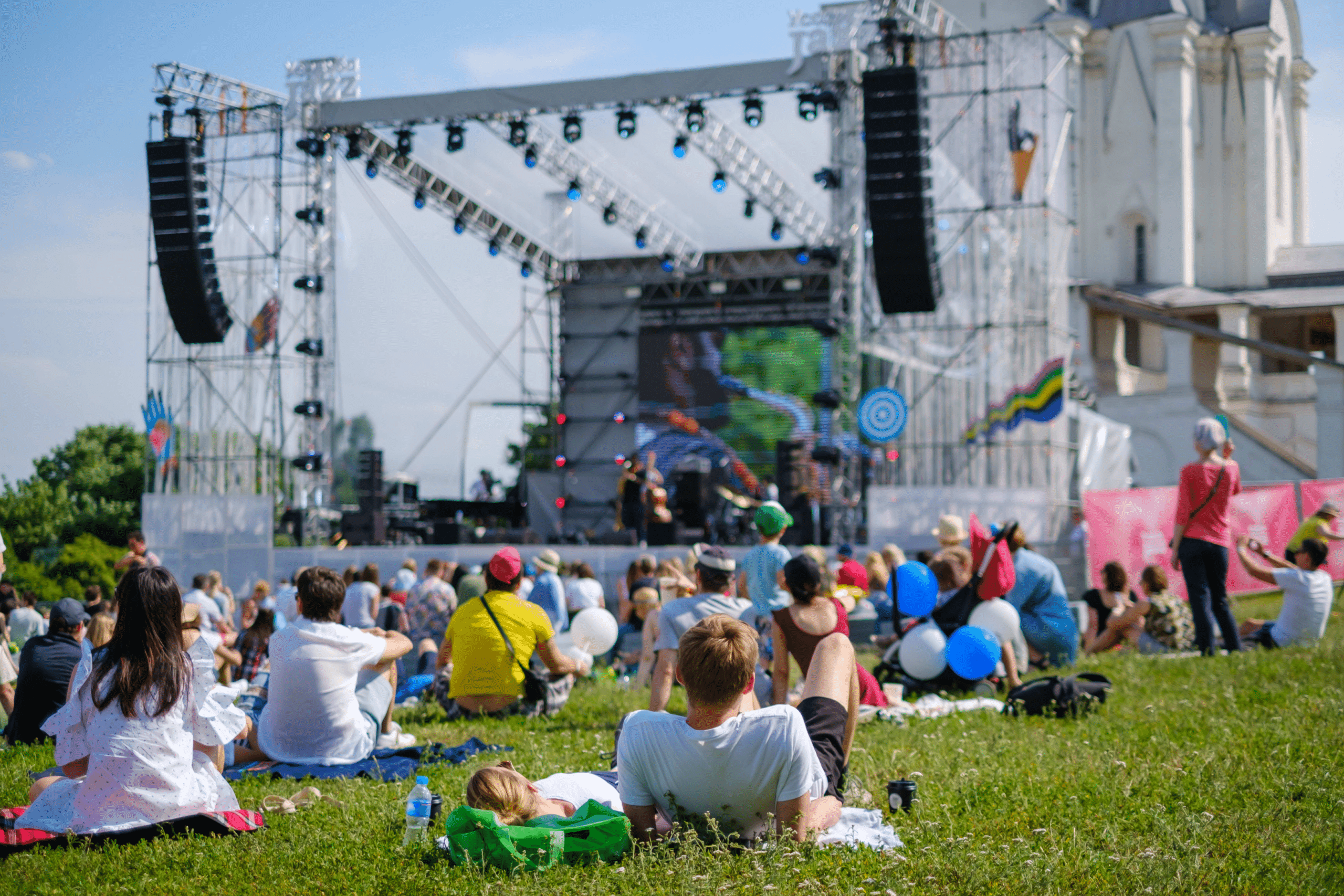 people sitting in the grass watching a concert on a big stage