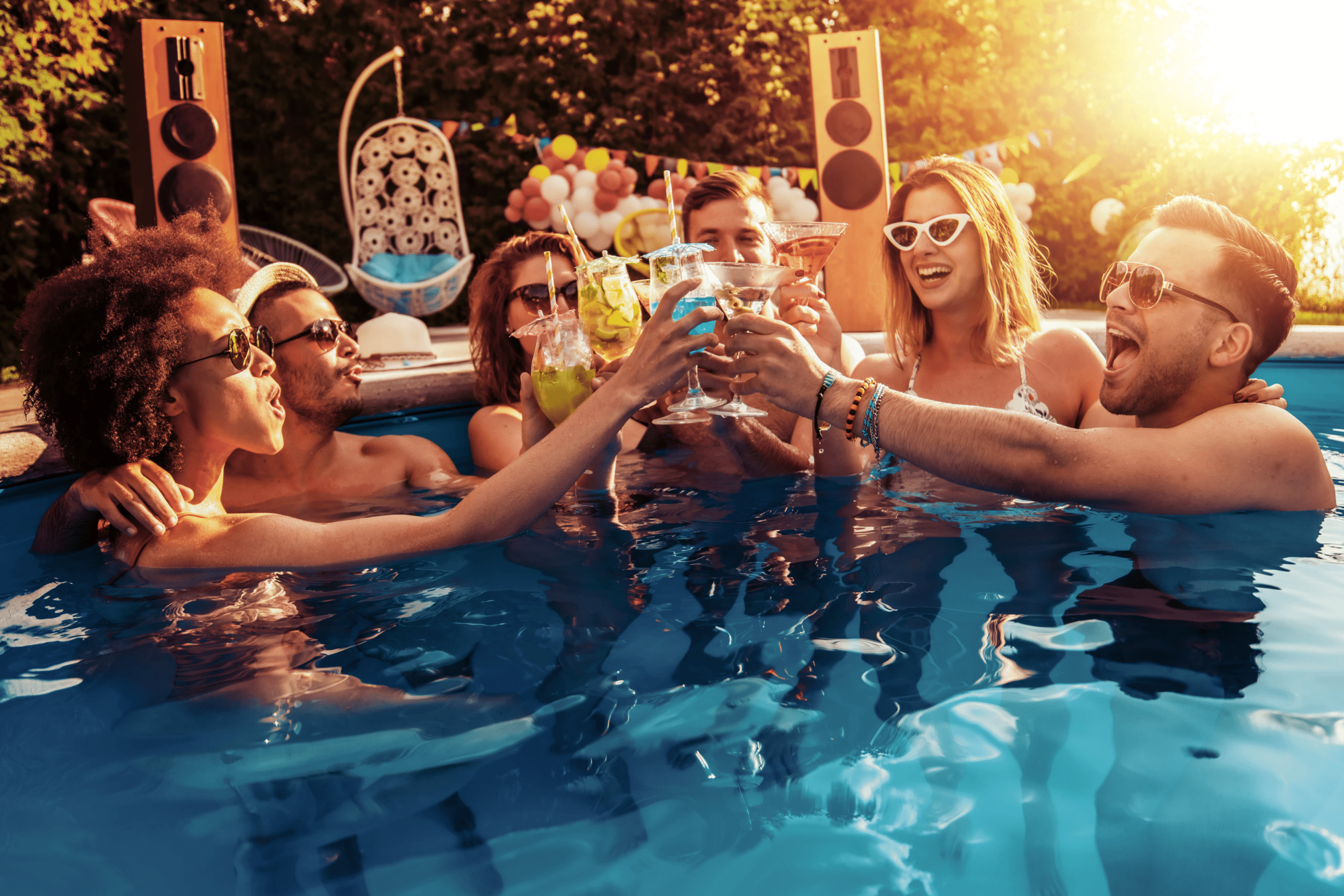 group of young people at a pool party clinking their drinks