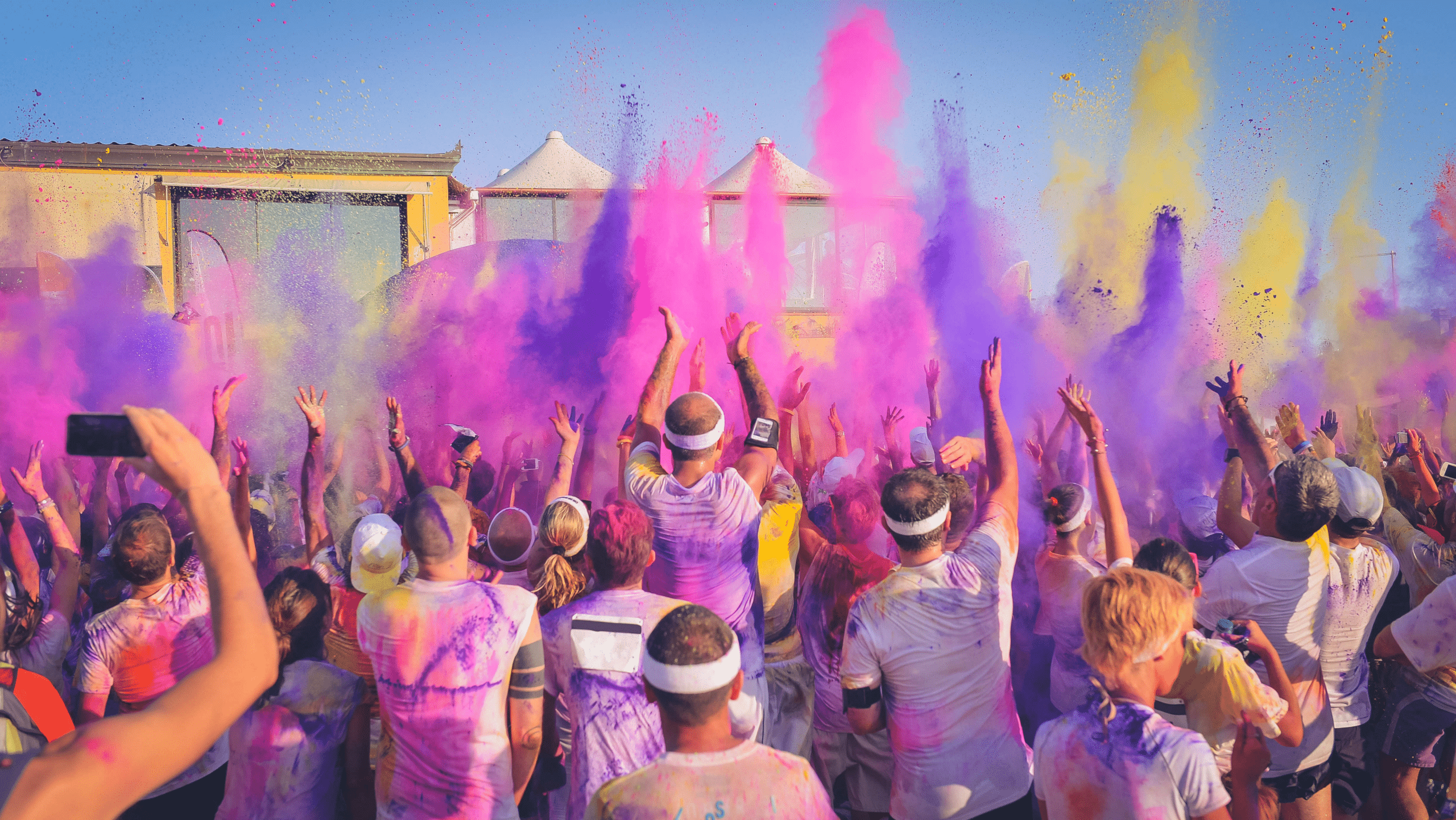 group of runners covered in yellow, purple, and pink powder from a color run