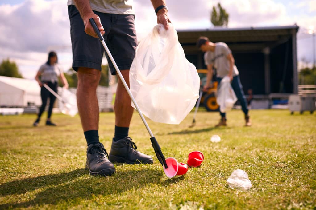 Close Up Of Volunteers Picking Up Litter After Outdoor Event Like Concert Or Music Festival