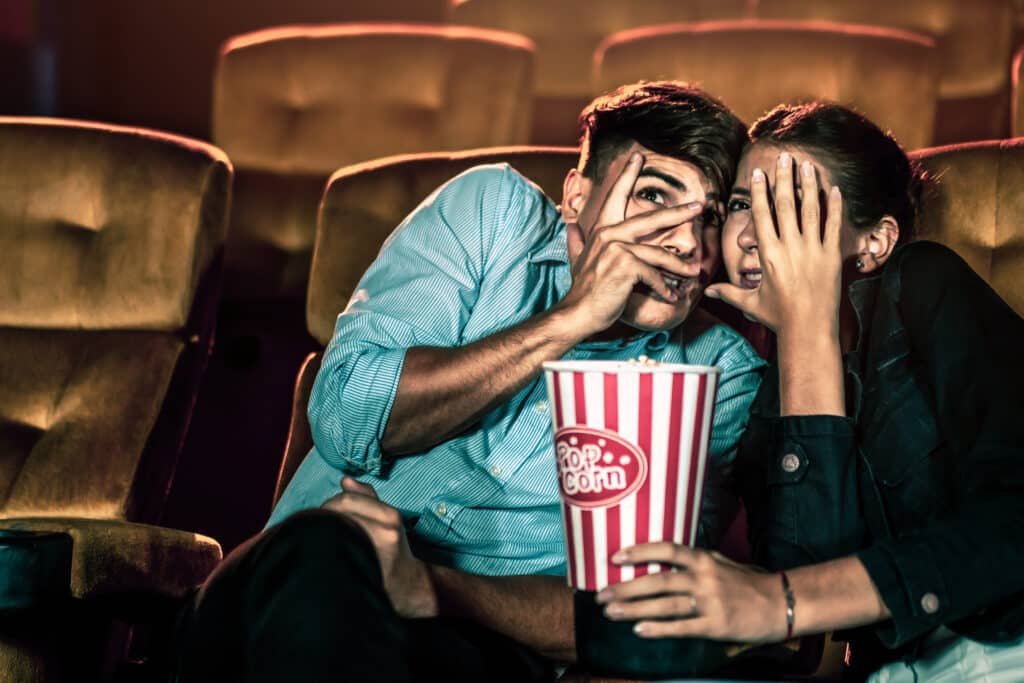 A couple watching a movie in shock and with their eyes closed in the movie theater cinema.