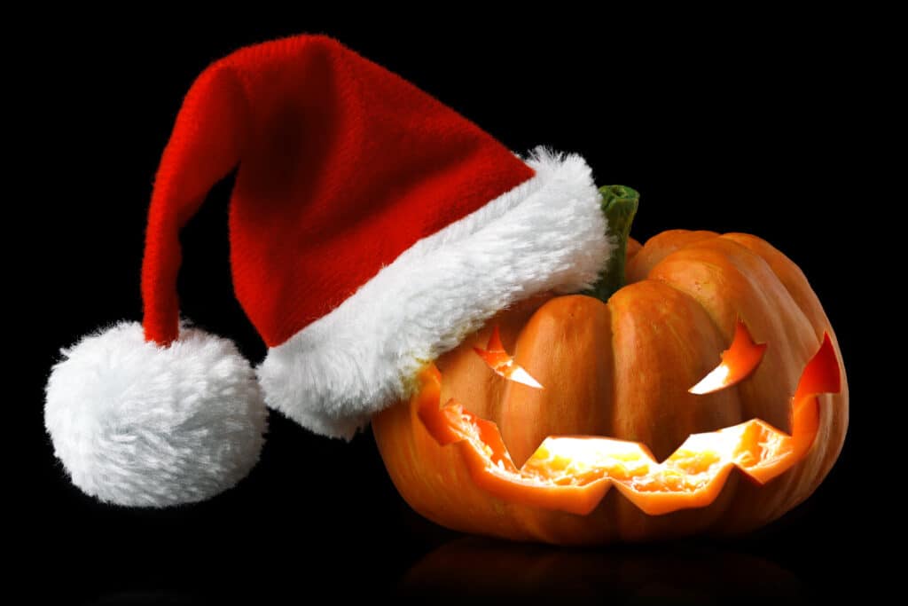 Single orange pumpkin Jack-o-lantern with Christmas Santa hat isolated on black background
