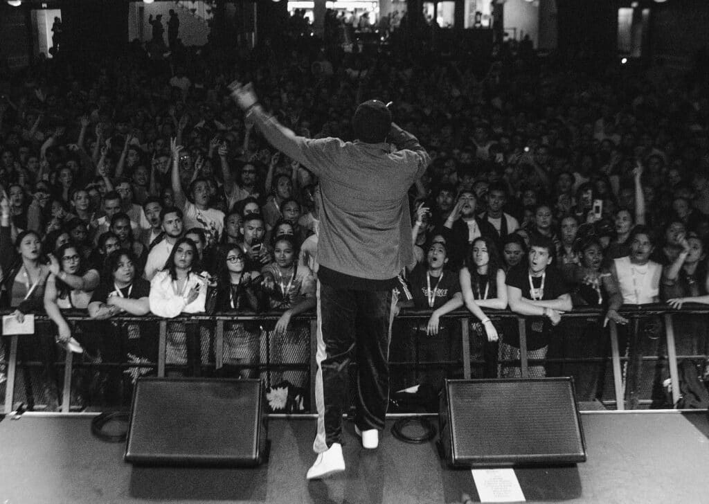 Black and white photo of B Wise singing to a large crowd