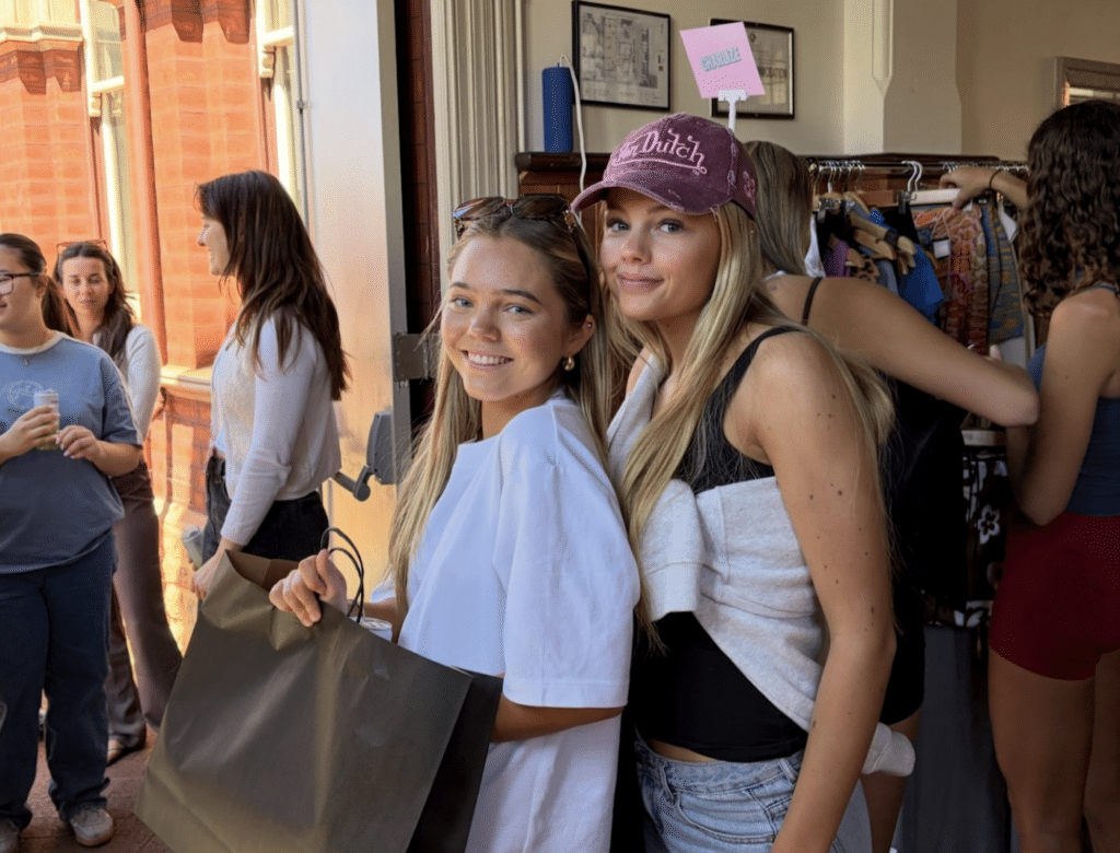 two girls posing and holding shopping bags in front of the clothing racks at the influencer rack sale