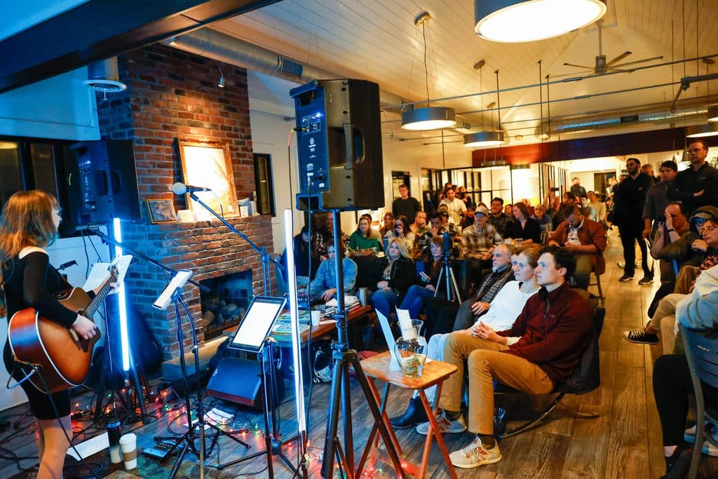 room full of fans in a coffee shop watching a female singer named Aisley Autumn perform with her acoustic guitar